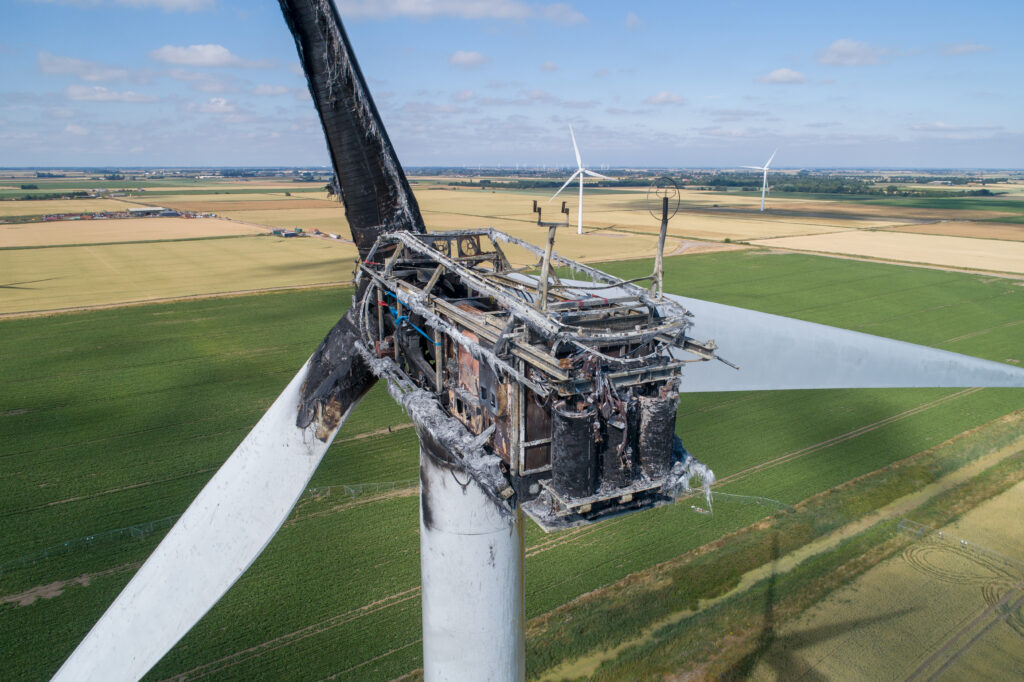 Aerial view of a damaged wind turbine with a burned-out nacelle after a fire.