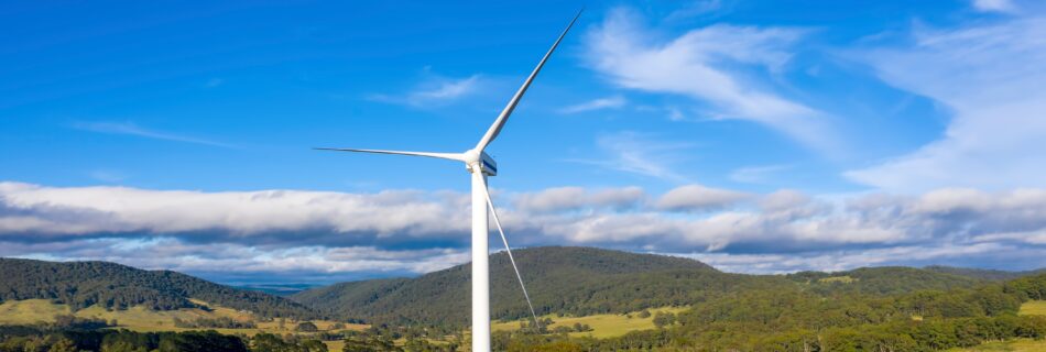 Wind turbine against a partly cloudy sky with rolling hills in the background.