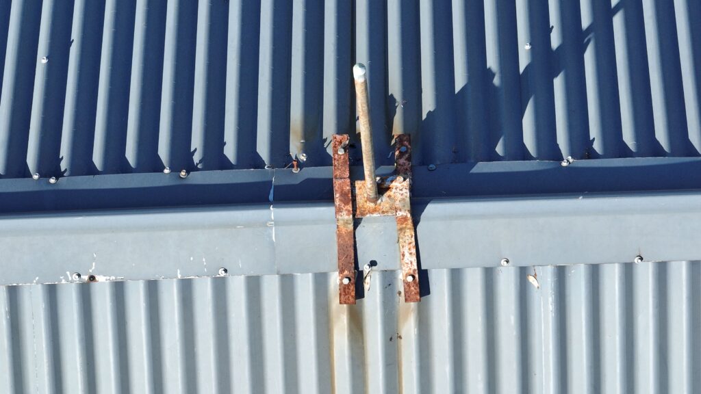 Corroded metal cross attached to a corrugated metal wall with shadows of palm leaves.