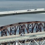 Two adjacent bridges, one a modern suspension bridge and the other an older truss bridge, with vehicles traveling across.