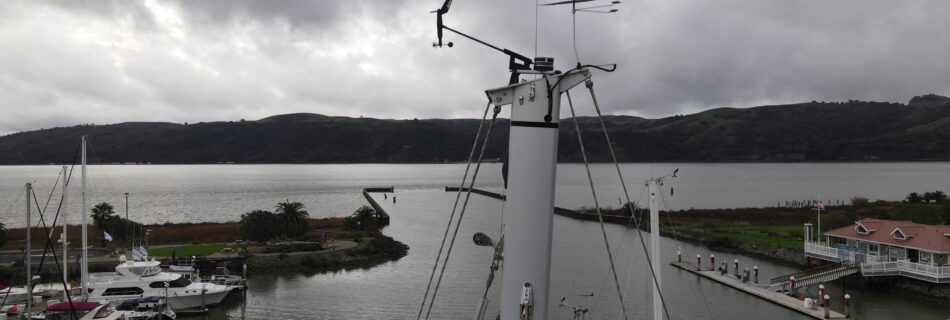 Overcast sky overlooking a marina with boats and a green hillside in the background.