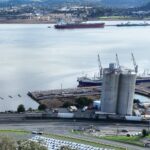 Aerial view of an industrial waterfront with ships, silos, and docked areas.