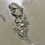 An aerial view of a small, rocky island surrounded by water with visible remnants of old, decayed wooden structures.