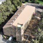 Aerial view of a large stone building surrounded by trees with multiple air vents on the roof.