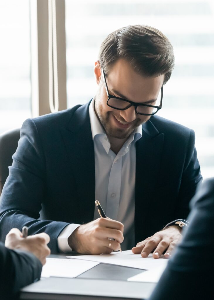 Man in a suit signing a document at a meeting.