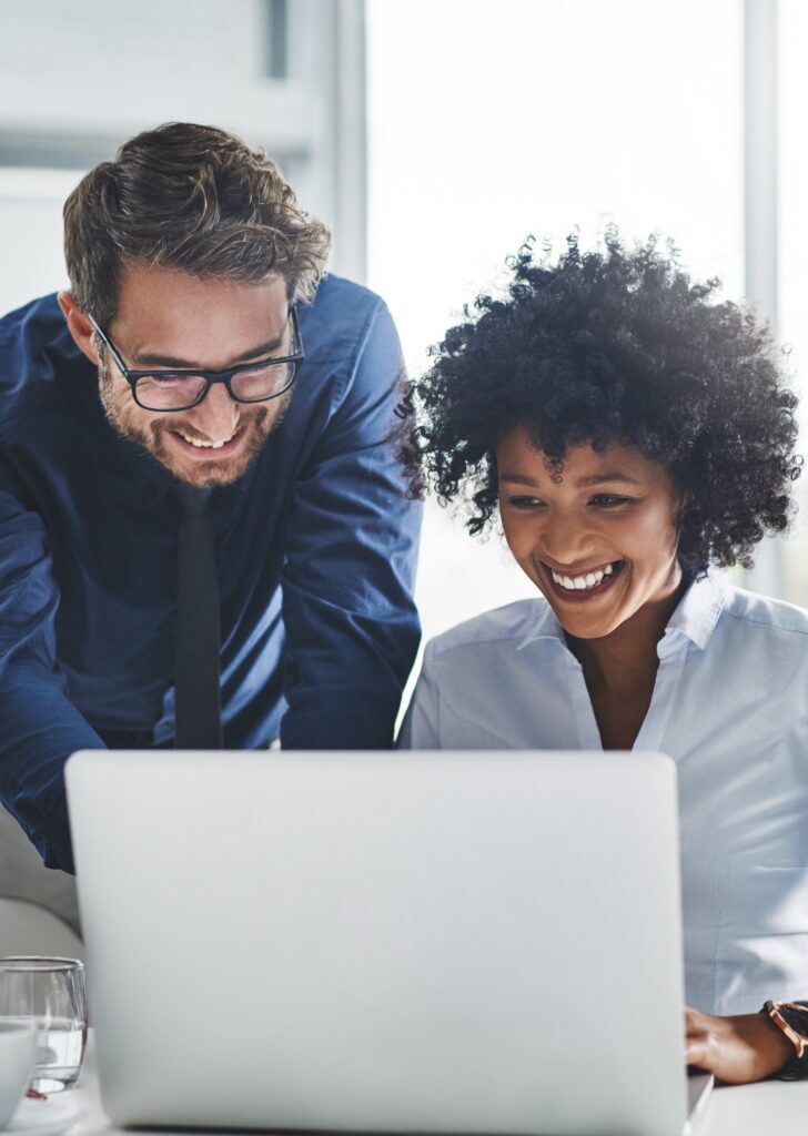 Two professionals smiling and looking at a laptop screen.